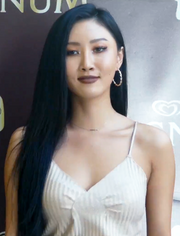 Hwasa wears a gray shirt against a branded brown backdrop