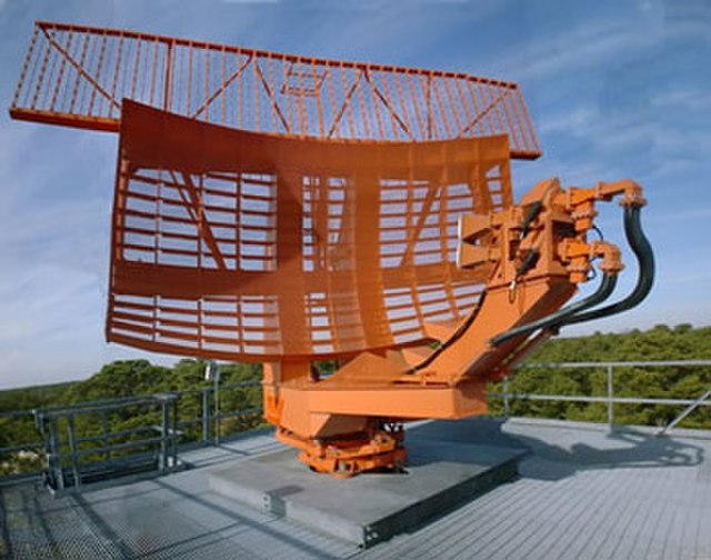 The parabolic antenna (lower curved surface) of an ASR-9 airport surveillance radar which radiates a narrow vertical fan-shaped beam of 2.7–2.9 GHz (S