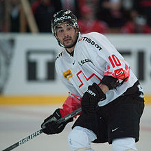 Кавказский хоккеист с шайбой выше колен. На нем красно-белый свитер с черным шлемом.