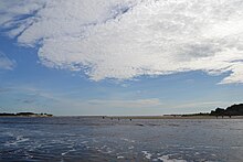 A view of the Carolina Beach Inlet at low tide, facing east from the Intracoastal Waterway. The men to the center-right are casting throw nets for mullet. Masonboro Island is the high bluff to the left and Freeman Park is in the distance on the right. CBInlet2018.jpg