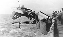 A U.S. Navy Curtiss SB2C-3 Helldiver caught in the after radio mast of the aircraft carrier USS Intrepid (CV-11) after a night landing accident on 30 October 1944. The plane was assigned to Bombing Squadron 7 (VB-7) aboard USS Hancock (CV-19).