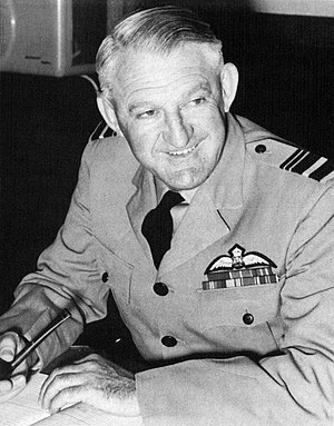 Half-length portrait of grinning man in military uniform, with pilot's wings on left breast pocket and pipe in left hand