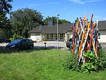 In the meadow there is a disordered bundle of wooden stakes as thick as arms, about three meters high, which are painted with colorful patterns.  The arrangement is reminiscent of a bundle of Mikado sticks before being dropped.