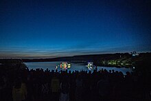 Floating stages lit up on lake at RSPB St Aiden's Floating stages lit up on lake, silhouettes of audience. Nest (play). LEEDS 2023.jpg