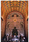 Interior photograph of a public area of the Guardian Building. Its high, arched ceilings are elaboraely patterned with brightly-colored designs, while an intricate metal screen partially hides a large mural behind.