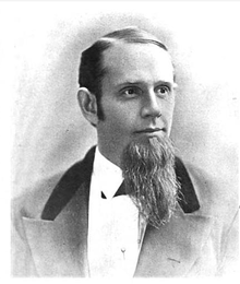 A middle-aged American gentleman of the immediate post-civil-war era. In this black-and-white portrait shot the subject looks to the viewer's right. His hair is short and sharply combed, and a magnificent beard is prominent on his chin. He wears a dark suit and white shirt.