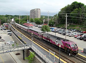 A purple and silver passenger train at a somewhat elevated station, viewed from above