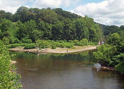 A body of water, seen from slightly above, that appears to fork in the center of the image. A metal bridge is partially visible crossing the right fork. The water in front is brownish, shading to green near the far shore. Some people are standing and fishing at the water's edge.