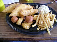 A typical meal from Long John Silver's: a platter with battered and fried fish and chicken, french fries (chips), battered fried shrimp, hushpuppies and coleslaw