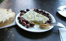 photographie d'assiettes : à gauche du pain, au centre du fromage blanc entouré d'olives noires