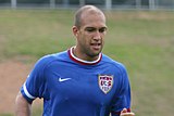 A photograph of a bald mixed-race man wearing a royal blue shirt.