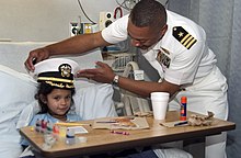 A U.S. Navy commander giving a hospitalized child his cap, bestowing her the title of "honorary ship's commander for a day". US Navy 061108-N-3750S-160 Cmdr. Brad Lee, commanding officer of USS San Antonio (LPD 17) places his cap on six year-old girl at Methodist Children's Hospital, making her an honorary ship's commander for a day.jpg