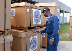 Humanitarian aid shipped in pallet boxes. Cover secured with strapping US Navy 080811-N-2821G-133 Culinary Specialist 2nd Class Paul Thomas, assigned to Commander, Task Force (CTF) 43, labels a box of Project Handclasp humanitarian aid supplies before storing it in the CTF-43 warehouse.jpg