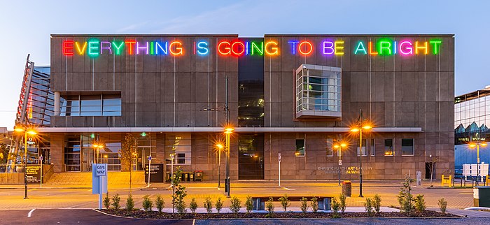 Sur un immeuble en lettres colorées majuscules est écrit le titre de l'exposition.