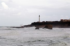 Vista de un punto rocoso coronado por un faro y que se adentra en el mar.