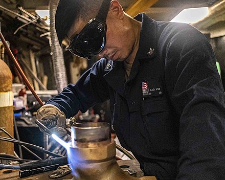 A US Navy maintenance technician torch brazes a steel pipe
