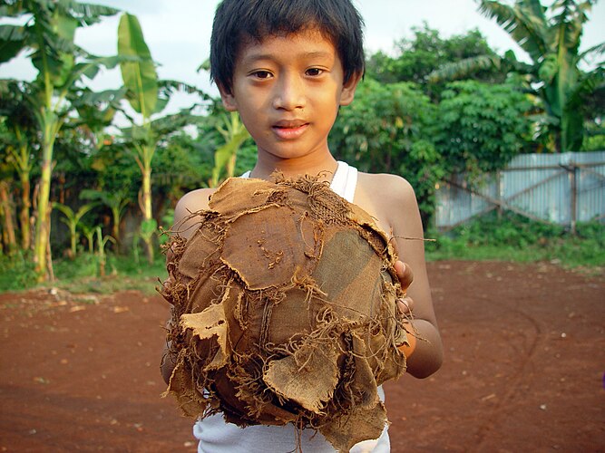 Мальчик в Джакарте (Индонезия) держит изодранный футбольный мяч