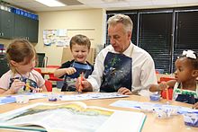 Drie kinderen en een volwassene zitten te schilderen aan een klaslokaaltafel.