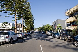 Street with parked cars and trees on both sides, surrounded by small buildings