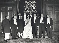 Um grupo formal de Elizabeth em tiara e vestido de noite com onze políticos em traje de gala ou em traje nacional.