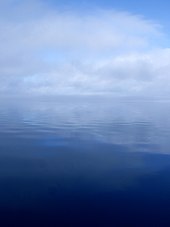 Eine ruhige, flache Flussoberfläche mit Wolken und Nebel, die die Horizontlinie verdecken