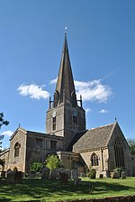 Église de pierre grise, au clocher pointu, sur fond de ciel bleu.