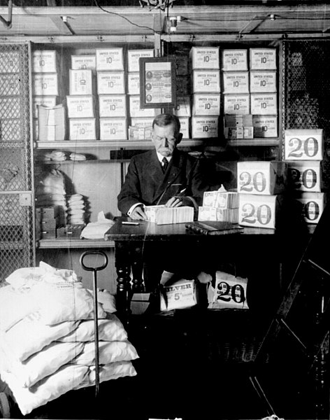 A Treasury Department official surrounded by packages of newly minted currency, counting and wrapping dollar bills in Washington, D.C. in 1907