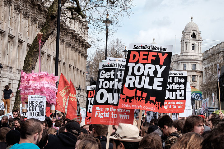 Manifestantes segurando cartazes, bandeiras e uma piñata em forma de porco fora de Downing Street. Imagem: Tom Morris.