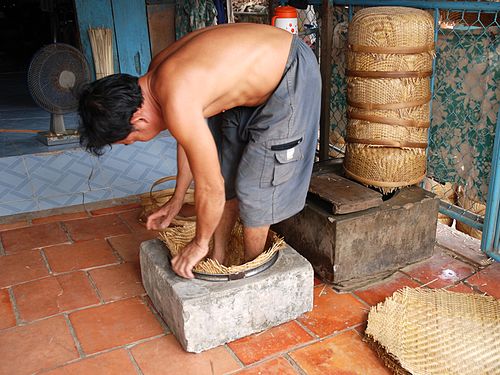 Basket maker in Mekong Delta, Vietnam, shaping the baskets from flat workpieces with his feet in some stone hollow.