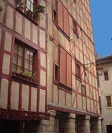 Photographie montrant une façade ocre aux pans de bois apparents peints en rouge.