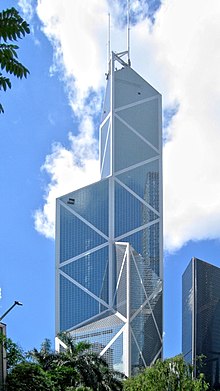 A tall tower coated with reflective glass and steel X patterns rises over trees and smaller buildings.