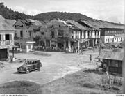 Photographie en noir et blanc d'un carrefour dans une ville après un bombardement : les quelques habitations sont délabrées.