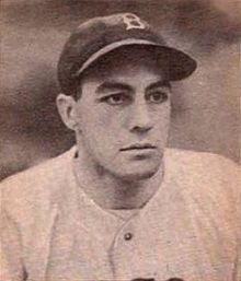 A man in a white baseball jersey and a dark cap with a white "B" on the center looks–the right.