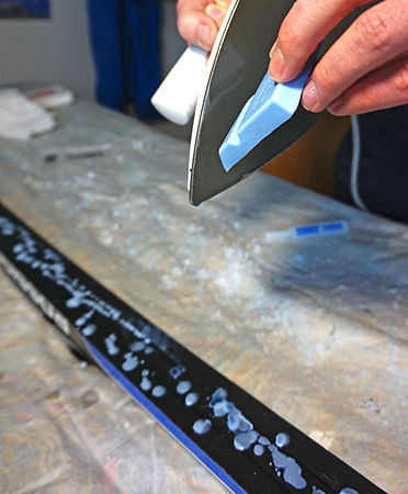 Melting glide wax onto a skate ski to be ironed in and scraped smooth.