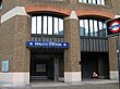 A brown-bricked building with a rectangular, dark blue sign reading "PIMLICO STATION" in white letters and a black sign reading "UNDERGROUND"