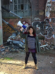 Sara Shaarawi stands in a derelict biscuit factory in Glasgow holding a Megaphone in a promotional image for the Workers Theatre. Sara Shaarawi Megaphone Image.jpg