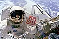 English: Astronaut Dale A. Gardner, having just completed the major portion of his second extravehicular activity (EVA) period in three days, holds up a "For Sale" sign refering to the two satellites, Palapa B-2 and Westar 6 that they retrieved from orbit after their Payload Assist Modules (PAM) failed to fire.