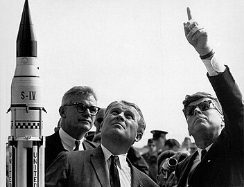 Középen elöl von Braun, tőle jobbra Kennedy elnök, a háttérben Robert Seamens – balra egy Saturn I rakétamodell látható