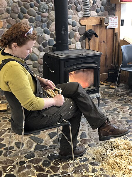 File:A Woodworker Whittling in Front of a Wood Stove.jpg