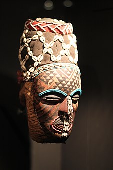 Ngady-Mwash mask; 19th century; Ethnological Museum of Berlin (Germany). The colors, red, brown & beige create a warm atmosphere of a savanna, being in contrast with the rows of blue beads. Like many other Kuba masks, this one is decorated with cowrie shells. Like many Kuba types of masks, ngady-mwash mask is extensively polychromed, or multicolored