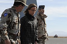 Femme entourée de deux soldats sur un aéroport militaire.