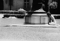 Charlotte Darehshori takes refuge behind a flagpole as an injured student, Devereaux Huffman, lies beside a hedge Charlotte Darehshori Hiding Behind Flagpole.jpg