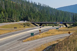 A simple overpass over a divided highway seen from a grassy area on the side of the road