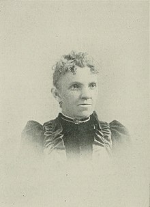B&W portrait photo of a middle-aged woman with her hair in an up-do, wearing a high-collared dark blouse.