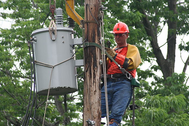 Lineworker replacing a transformer, wearing protective gear, including rubber gloves and sleeves