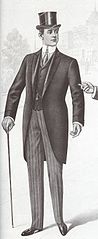 Morning dress with grosgrain lapels, matching black waistcoat with a then-fashionable shorter skirt length, top hat, formal gloves, contrasting-top Oxford boots with punching across the toe cap, boldly striped long tie, striped shirt with contrasting white turn-down collar and cuffs, and striped formal trousers. The characteristic angle of the cutaway front of the skirt is clearly visible, as is the waist seam. (May 1901)