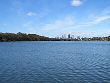 A lake with a city skyline in the background and trees to the left