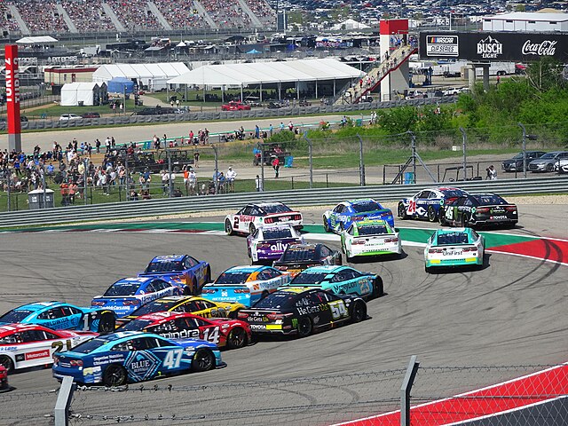 Many stock cars going into the first turn at Circuit of the Americas