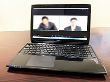 A laptop is sitting on a desk, the screen is divided in half showing a two blurred images of two people video conferencing.