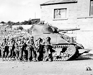 Combined arms in action: a WWII tank (M4 Sherman shown) was effective against wide range of targets but needed support of infantry to protect it against close attacks Yanks advance into a Belgian town.jpg